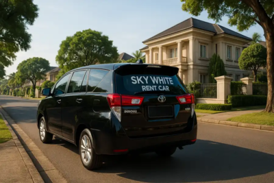 Toyota Innova hitam bersih, terparkir di tepi jalan perumahan elite Pancoran Mas, Kota Depok. Terdapat watermark tulisan "Sky White Rent Car" di kaca belakang mobil. Pemandangan langit cerah dan pepohonan hijau sekitar memperkuat nuansa profesional dan elegan layanan rental mobil.